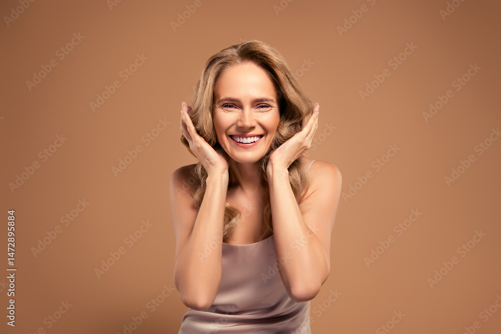Fototapeta premium Smiling mature woman showcasing elegance and vitality against beige background, emphasizing beauty