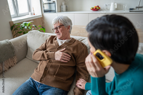 Struggling retired man in pain with chest discomfort, wife call ambulance assistance. Medical alert, emergency call, cardiac attack infarct concern, caregiving response, aging health crisis at home