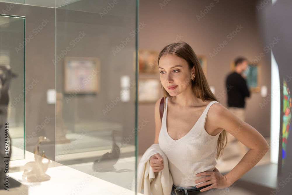 Beautiful woman looks with interest at a glass showcase with a museum exhibit. European woman examines works of art Beautiful woman looks with interest at a glass showcase with a museum exhibit. European woman examines works of art