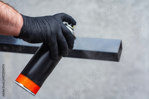 Obraz na plátně Close-up of a hand wearing a black glove spraying paint from a black aerosol can onto a metal surface