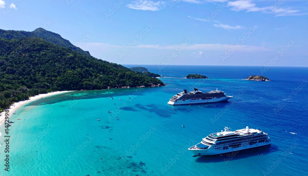 Fototapeta premium Coastal view with two ships docking near a beach under a clear, bright sky
