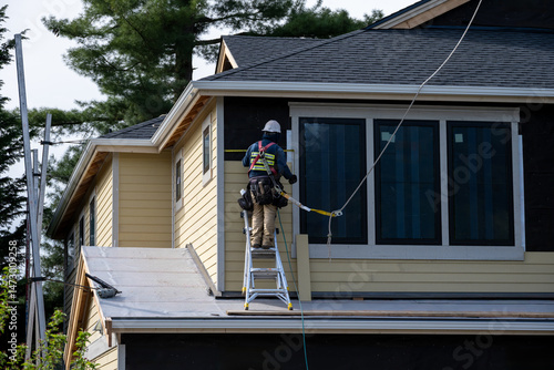 Behang Carpenter on ladder installing wood siding 2nd floor exterior wall on new home c