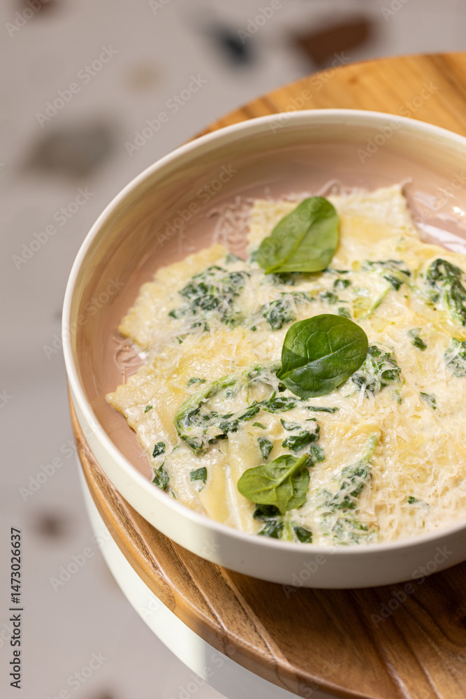 Fototapeta premium Spinach Ravioli with Creamy Parmesan Sauce. Fresh ravioli pasta filled with spinach, topped with creamy cheese sauce and garnished with spinach leaves in a modern bowl.