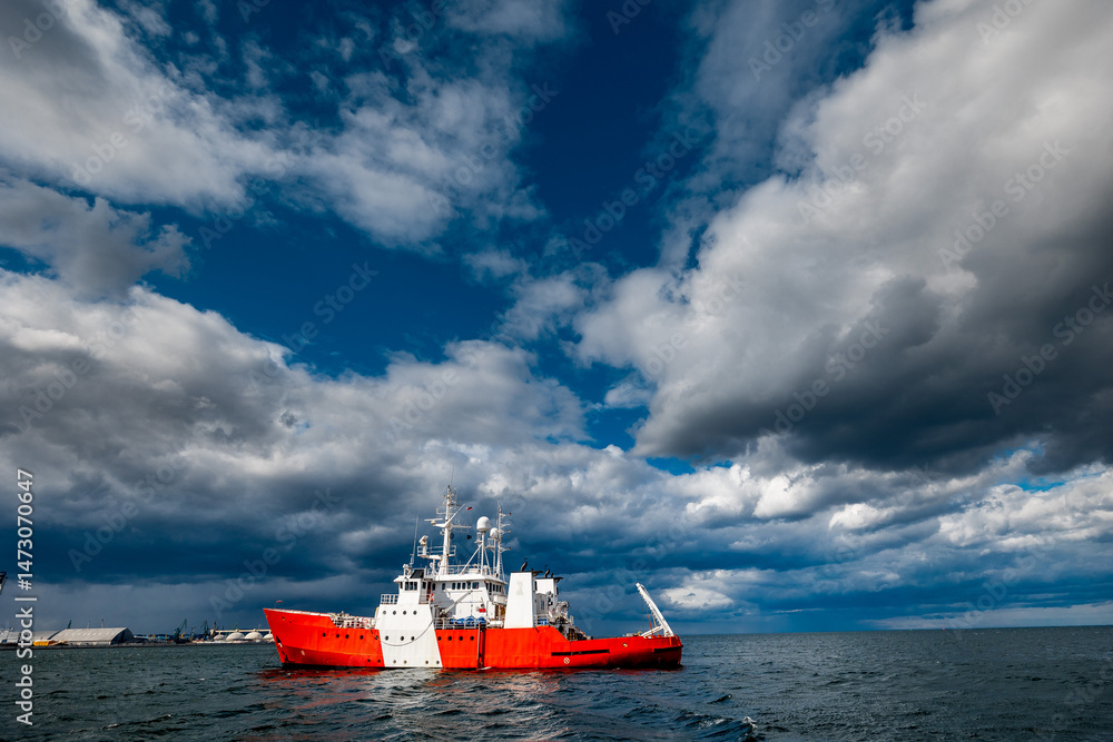 Fototapeta premium Red and White Coast Guard Ship on Open Sea Under Dramatic Stormy Sky, Port of Gdynia, Poland