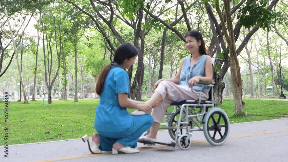 Elderly woman sitting in a wheelchair and being cared for by a female nurse in the park, natural therapy concept Staff or caretakers of the elderly Elderly woman sitting in a wheelchair and being cared for by a female nurse in the park, natural therapy concept Staff or caretakers of the elderly