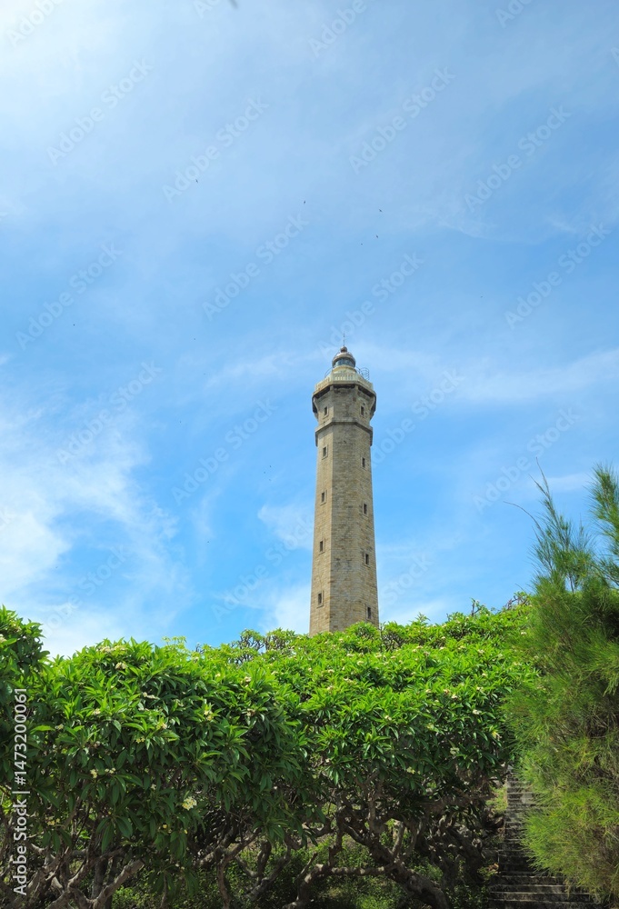 The Ke Ga Lighthouse in Vietnam stands tall above lush green foliage under a bright blue sky. The Ke Ga Lighthouse in Vietnam stands tall above lush green foliage under a bright blue sky.