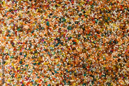 Vivid surface full of mixed gems, pearls, and beads. Decorative stones in rich hues create a shiny and artistic natural background