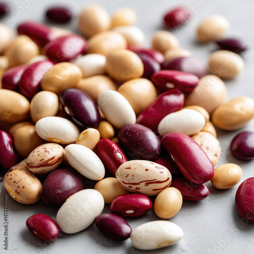 A colorful assortment of dried beans, showcasing various sizes, shapes, and hues.  The beans are scattered on a neutral-toned surface