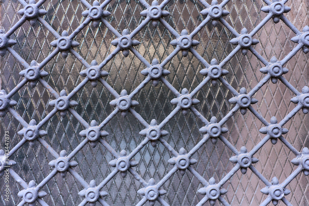 Fototapeta premium Decorative metal lattice with geometric and floral elements over diamond-patterned textured glass, creating a detailed and symmetrical architectural motif.