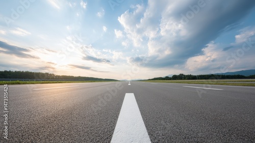 A low angle view captures an empty highway leading into a captivating horizon, adorned with colorful clouds during sunset, creating a serene landscape