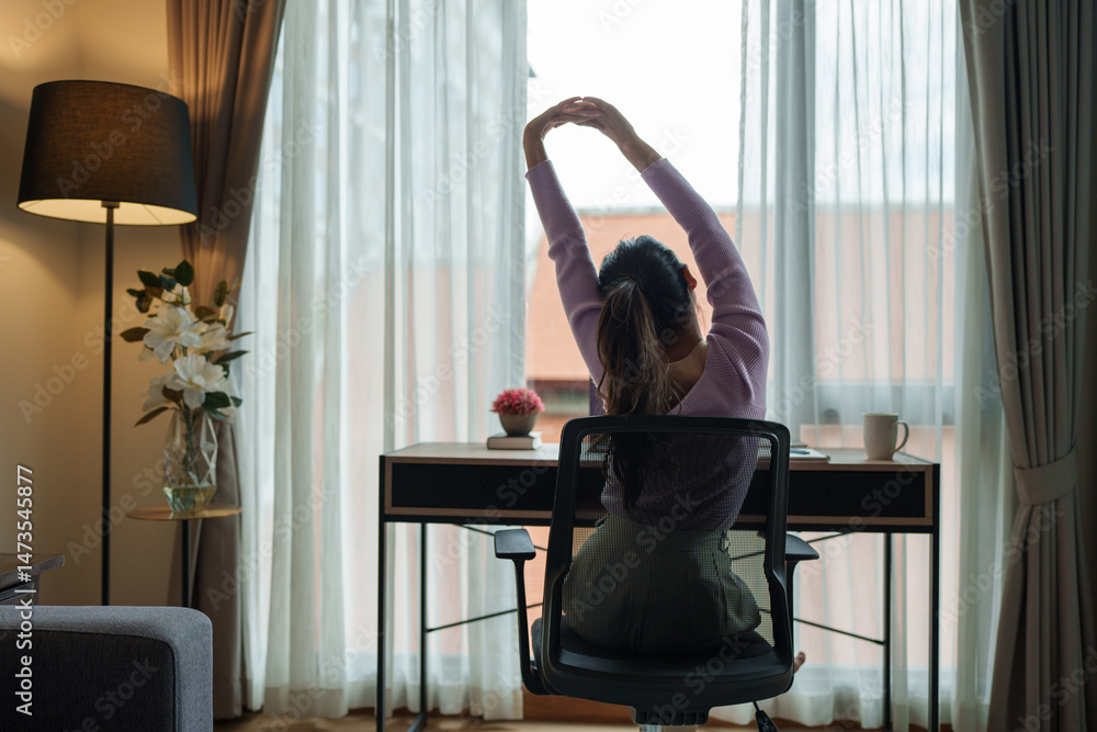 Obraz premium Young woman stretching at home office desk after work