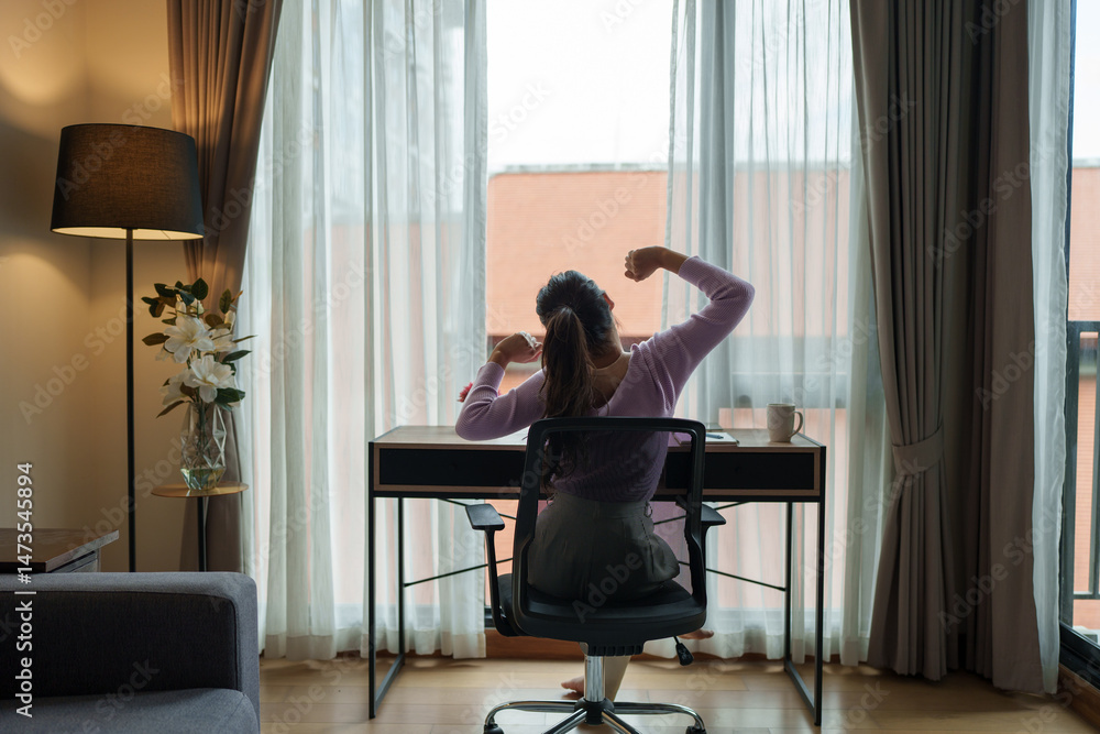 Fototapeta premium Young woman stretching at home office desk after work