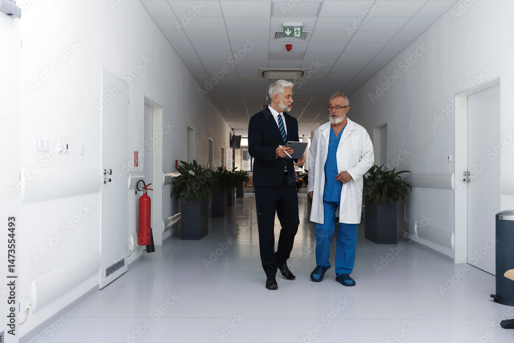 Fototapeta premium Doctor talking with hospital manager, walking down hospital hallway.
