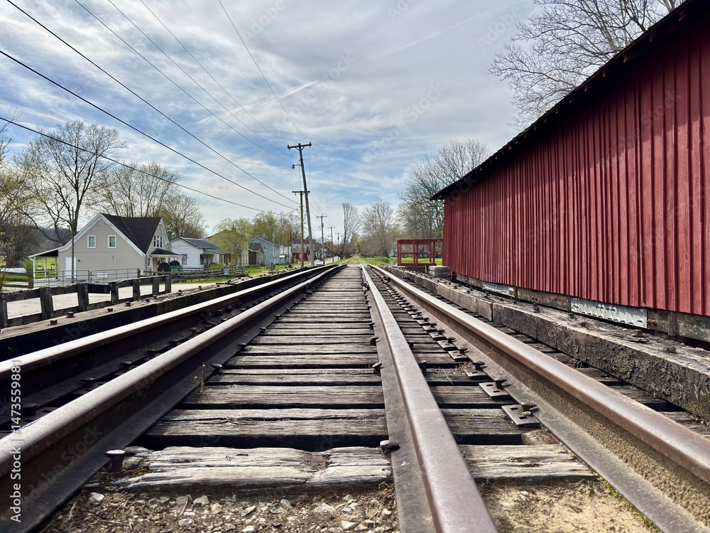 Fototapeta premium Railroad tracks beside red covered bridge running through small town