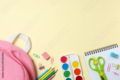 A pink backpack with school supplies placed against a beige yellow background