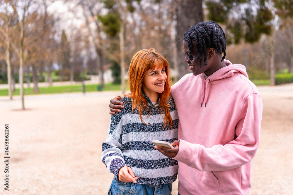 Obraz premium Young couple smiling and using smartphone in park