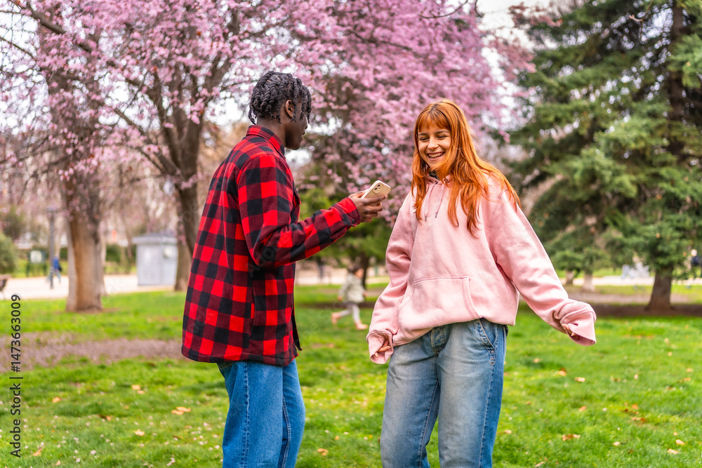 Young man filming dancing woman with smartphone in spring park Young man filming dancing woman with smartphone in spring park