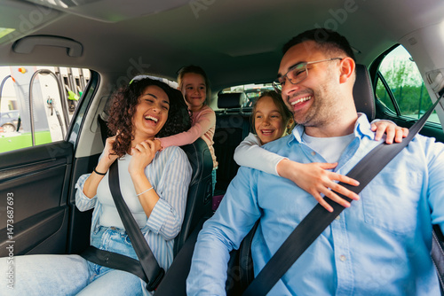 Cheerful family traveling in a modern electric car, enjoying laughter and fun during their road trip. Daughters wearing seatbelts, creating joyful memories together