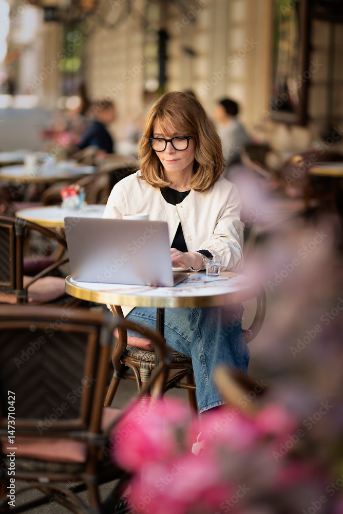 Obraz premium Mid aged businesswoman sitting at outdoor cafe and working on her laptop