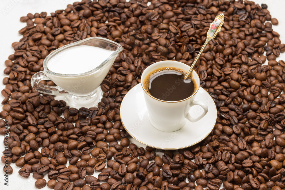 Fototapeta premium Cup of coffee and cream among roasted coffee beans.