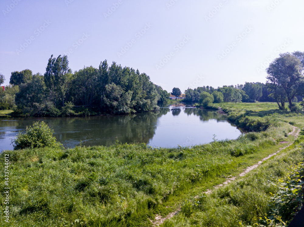 Landscape with grass field, river and blue sky