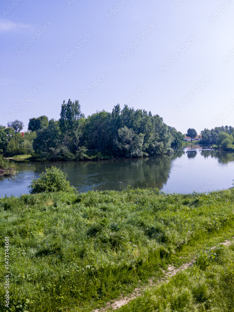 Landscape with grass field, river and blue sky