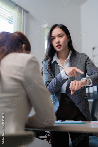 Canvas Print Impatient manager is pointing at her watch while talking with her employee durin