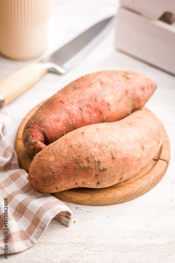 Raw sweet potatoes on cutting board on white table.