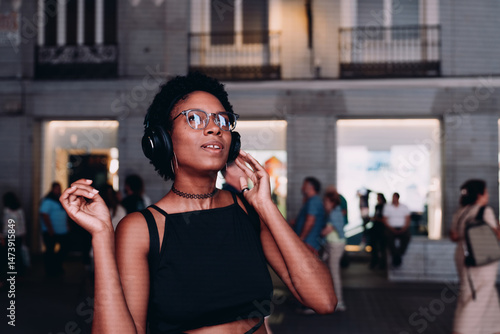 Fotografie Young African American woman enjoying immersive sound through headphones in city