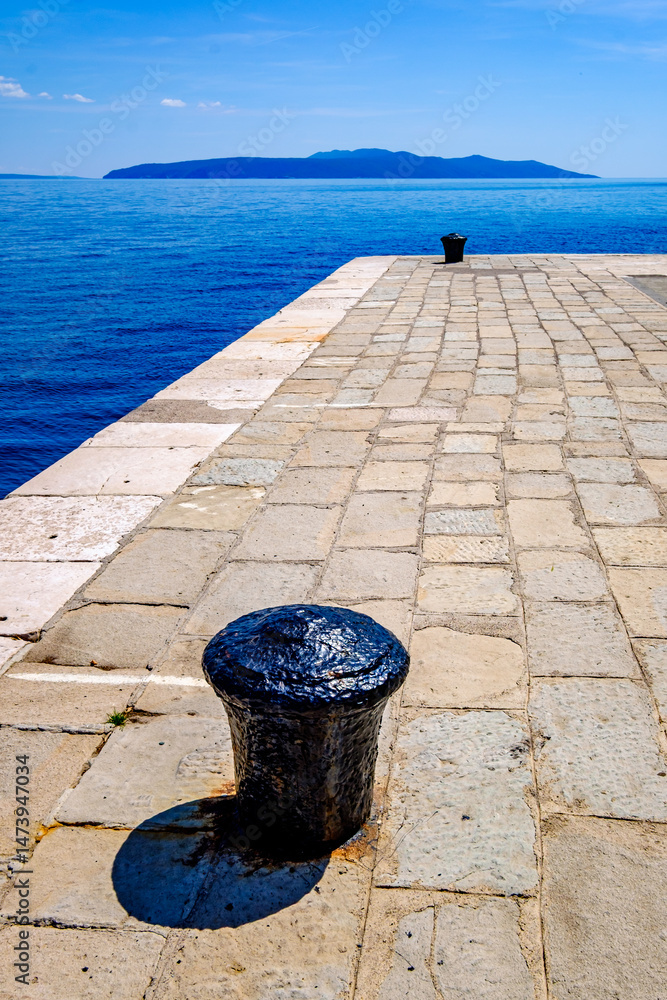 Obraz premium Dockside view of a sturdy bollard overlooking the calm blue waters, capturing a serene coastal moment in a picturesque harbor setting