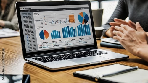 Office laptop displays data charts; meeting background