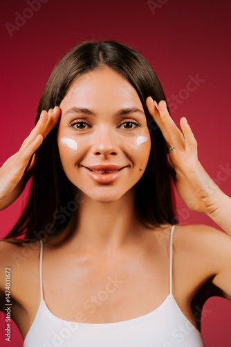 Wallpaper Mural Woman applying skincare product on face with a joyful smile in a vibrant setting Torontodigital.ca