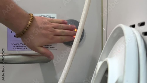 Horizontal video. Public restroom on long distance train. Male hand presses touch flush button with led lamp. Text on wall. Translation from Armenian and Russian: Do not use toilet when light is red