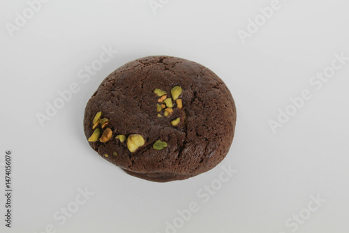A chocolate soft cookie, with green pistachio topping, isolated on white background