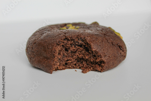 A bitten chocolate soft cookie, with green pistachio topping, isolated on white background