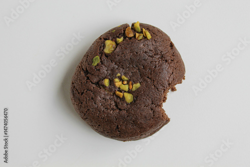 A bitten chocolate soft cookie, with green pistachio topping, isolated on white background, flat lay or top view