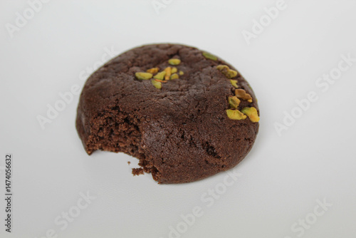 A bitten chocolate soft cookie, with green pistachio topping, isolated on white background
