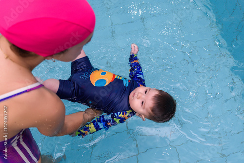 Swimming instructor holding baby floating in water during early stimulation class