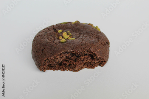 A bitten chocolate soft cookie, with green pistachio topping, isolated on white background
