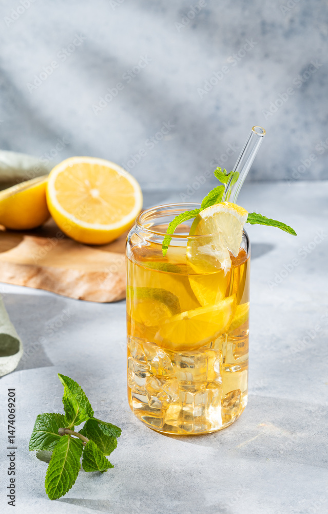 Fototapeta premium Iced drink with lemon and mint in a glass on light background with shadows and citrus fruits.