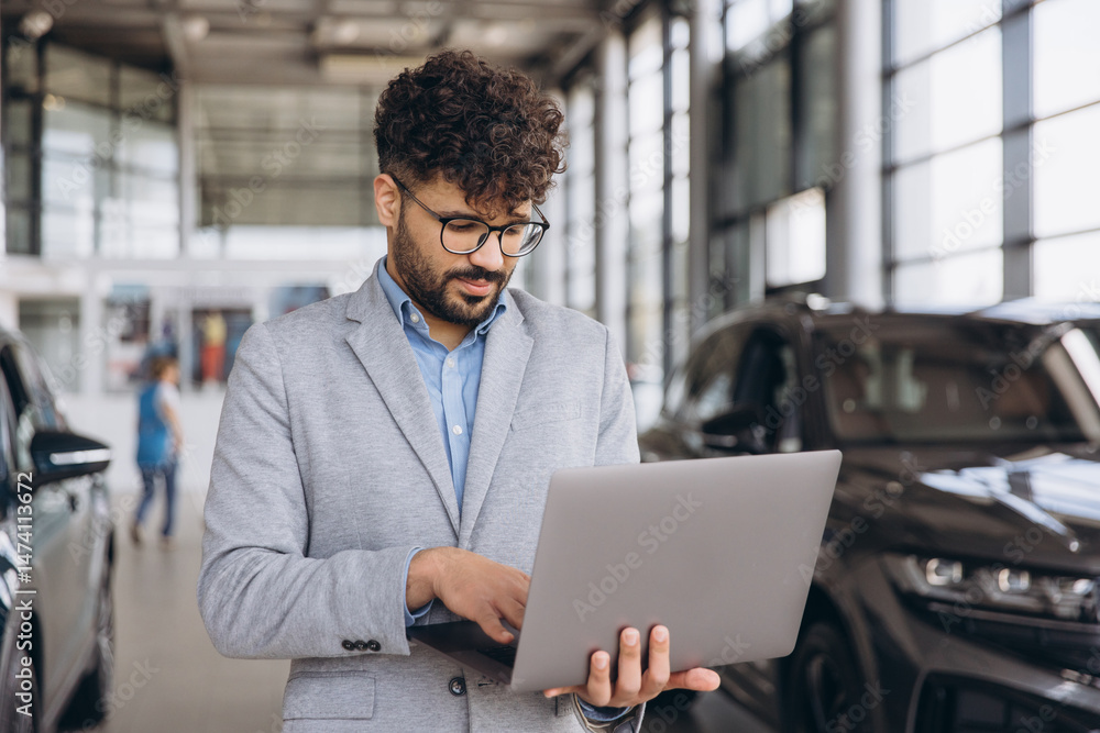 Car salesman working on laptop in car dealership Car salesman working on laptop in car dealership