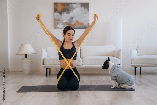 Yellow tape, stretching. Woman with pug dog is doing yoga at home