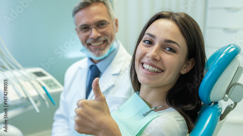 Happy client in dentist's office recommending dental clinic satisfied with good service provided by hygienist. Smiling female patient giving thumbs up and looking at camera during regular checkup