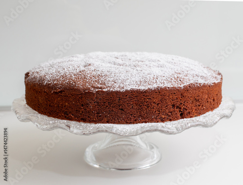 Delicious caprese cake resting on elegant glass cake stand, sprinkled with powdered sugar