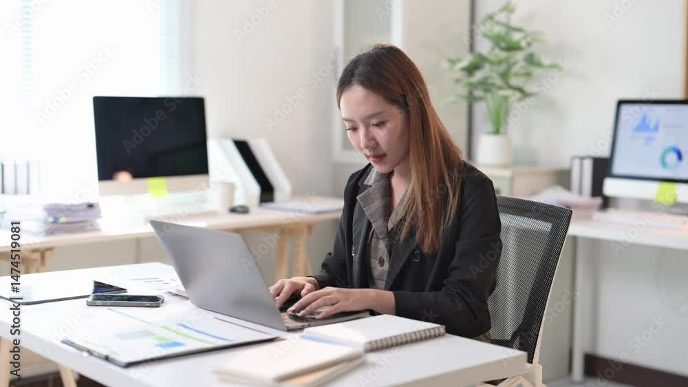 A woman is sitting at a desk with a laptop and a notebook. She is smiling and she is enjoying her work A woman is sitting at a desk with a laptop and a notebook. She is smiling and she is enjoying her work