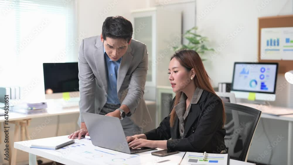 A man and a woman are in a business meeting. The man is pointing at a laptop screen A man and a woman are in a business meeting. The man is pointing at a laptop screen
