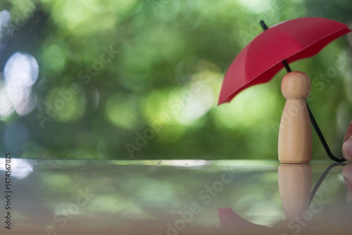 Wallpaper Mural One wooden figure stands protected under a red umbrella by human hand against a natural background, symbolizing safety and security. insurance and social protection patronage and mentoring Torontodigital.ca