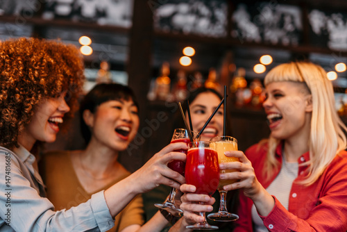 Sticker Cheerful female friends toasting cocktails at bar counter