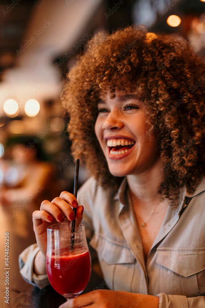 Fototapeta premium Happy young woman drinking red juice in restaurant bar and smiling