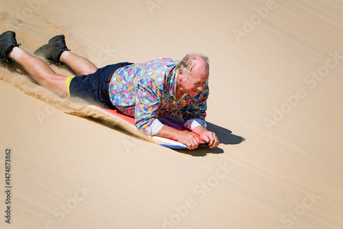 Bild auf Leinwand Older senior man sandboarding down sand dune on boogie board, retirement fun exc